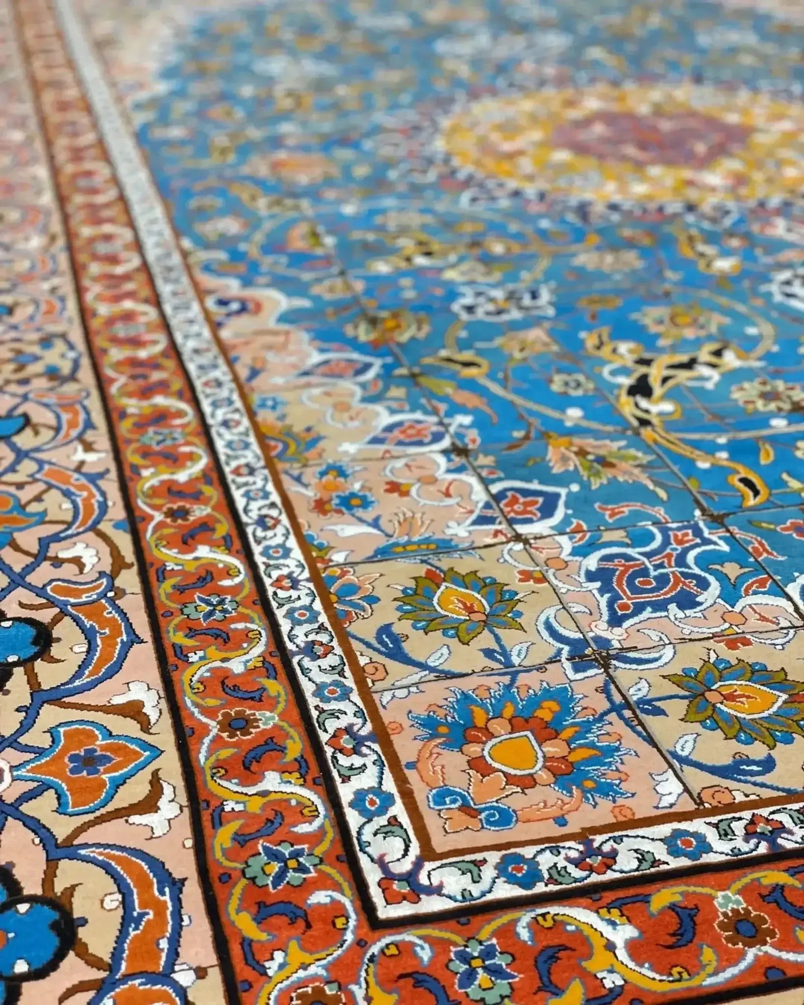 "Close-up of a Persian rug’s intricate border design, featuring vibrant floral and geometric motifs in blue, orange, and gold."